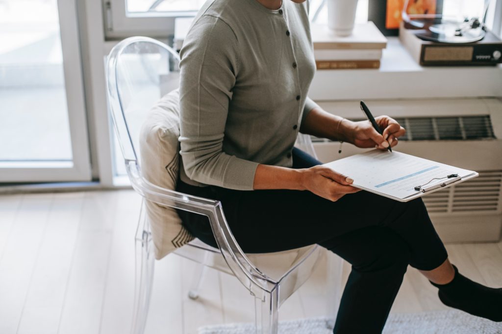 Person sitting on a chair, completing a survey on a clipboard.