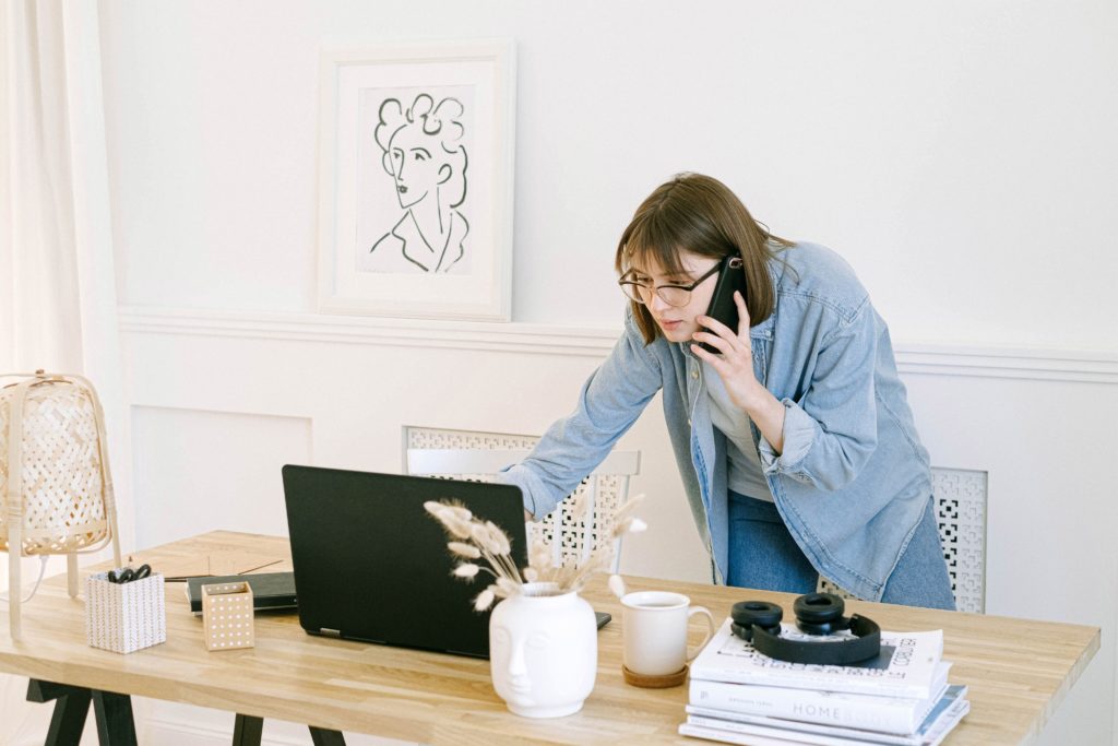 Woman leaning over a desk to look at a laptop screen while on the phone.